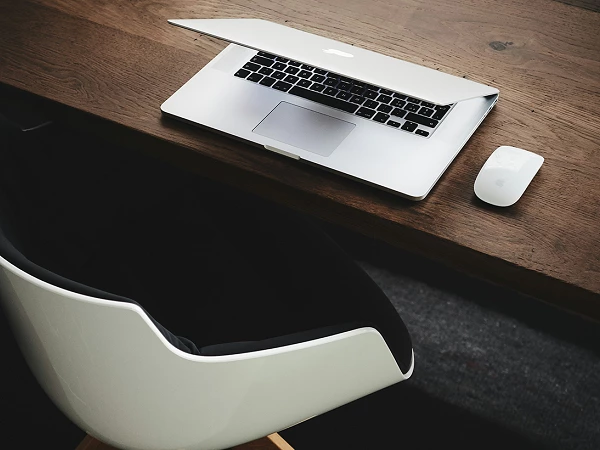 Teilgeöffnetes MacBook und Apple-Maus auf dunklem Holztisch