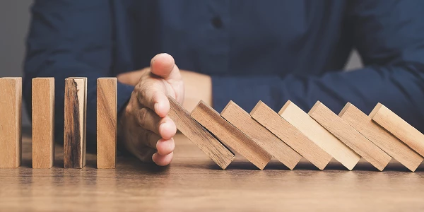 Hand stops falling wooden domino blocks on wooden table