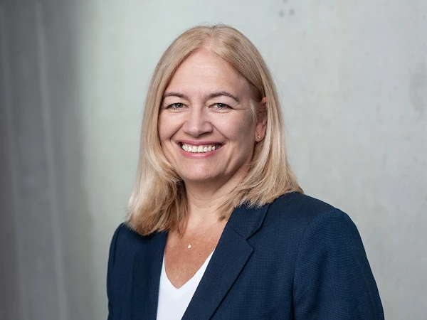 Frau mit blonden Haaren in blauem Blazer, lächelt freundlich in die Kamera