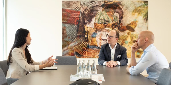 Drei Personen im Meeting mit Gesprächsthema, bunte Kunst im Hintergrund